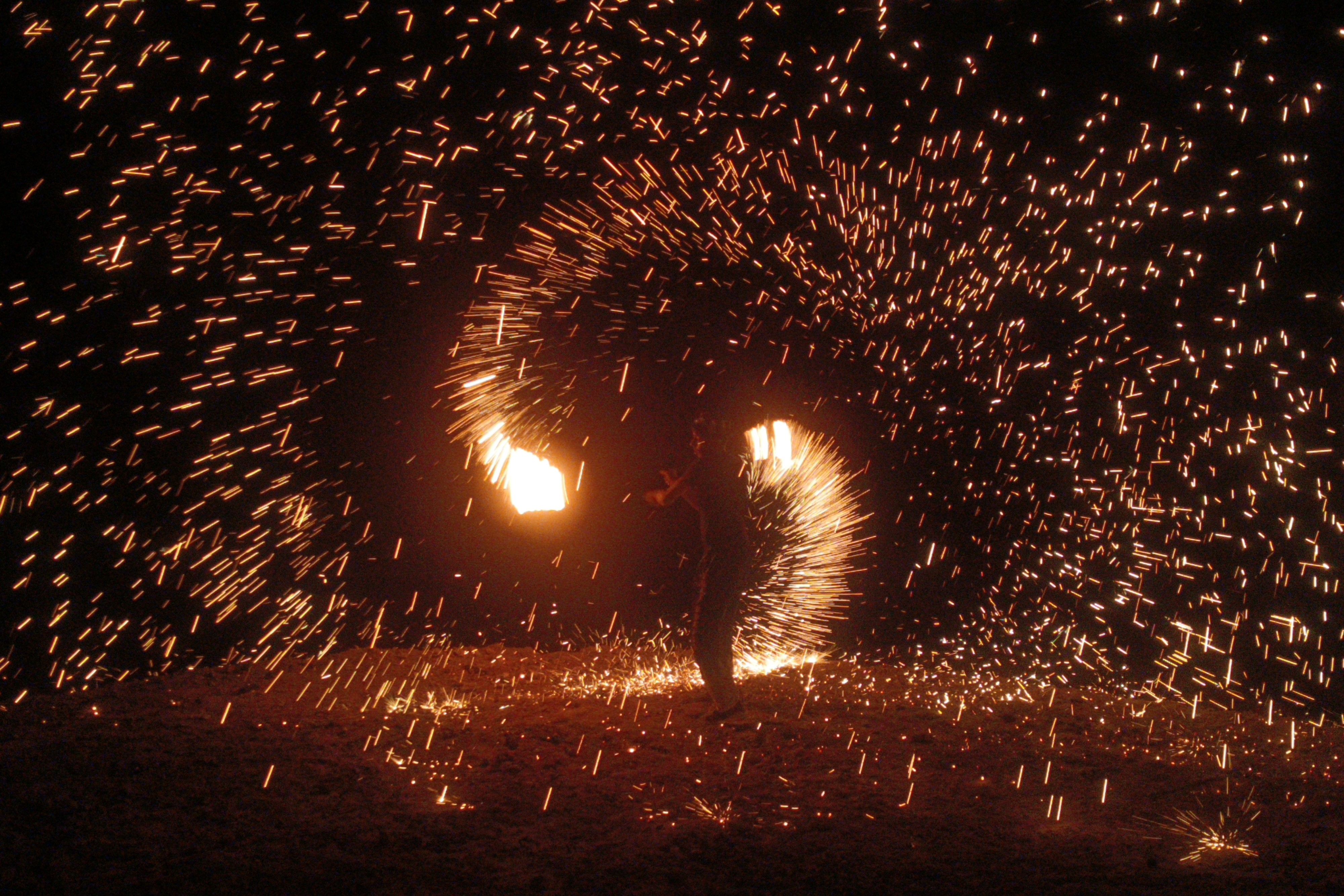 Fire spinning performance sending sparks in an arc across the desert camp at night